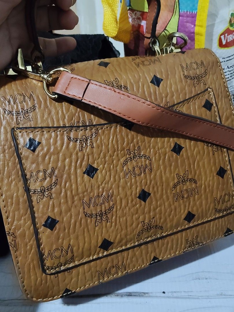 MCM Brown Leather Top Handle Shoulder Bag (Category: Luxury Bags & Wallets) located in Cebu City. Submitted by almzcorner (Listing ID 1469922805, Image 2). Description: - Brand: MCM - Material: Brown pebbled leather with signature monogram pattern - Details: Solid brown front pocket & gold-tone hardware with engraved branding - Interior: Red fabric lining with a zippered pocket and brand plaque - Inclusion: Matching adjustable shoulder strap incl