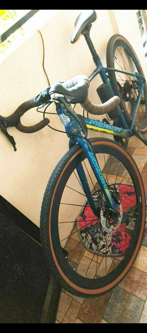 Merida Gravel Bike (Category: Bicycles) located in Las Pinas. Submitted by Rmtn14 (Listing ID 1469914796, Image 1). Description: - Brand: Merida Gravel Bike - Frame: Blue with eye-catching yellow and green graphics - Handlebars: Drop bars with stylish brown tape - Saddle: Black with a sleek orange accent underneath - Tires: High-grip knobby tires featuring classic brown sidewalls - Brakes: Front and rear disc brakes for reliable stopping power - 