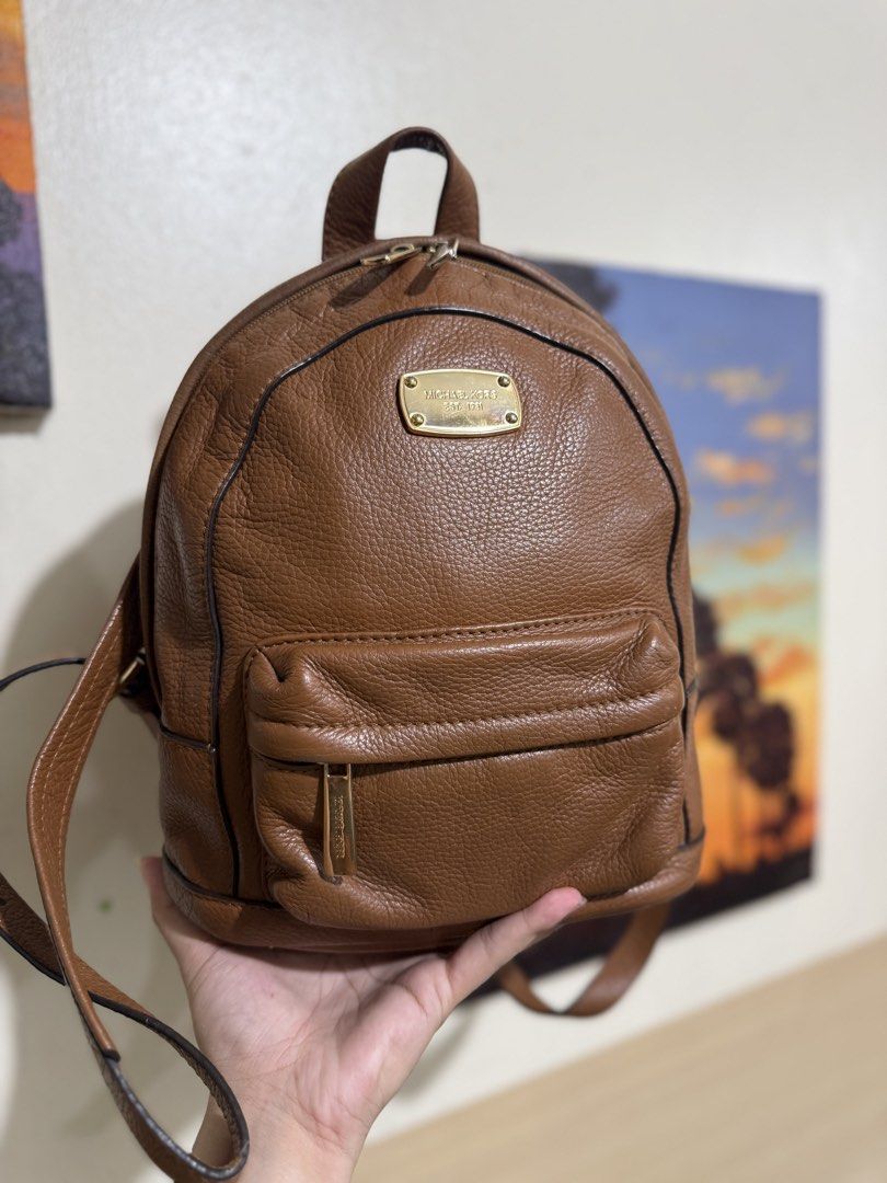 Michael Kors Brown Leather Backpack (Category: Backpacks) located in Quezon City. Submitted by vianca13 (Listing ID 1469817333, Image 1). Description: - Brand: Michael Kors - Material: Brown pebble leather with gold hardware - Straps: Top handle and adjustable shoulder straps - Pockets: Front zipped pocket, main compartment, interior zip pocket, and slip slots - Lining: Signature logo interior lining - Small to semi med size .