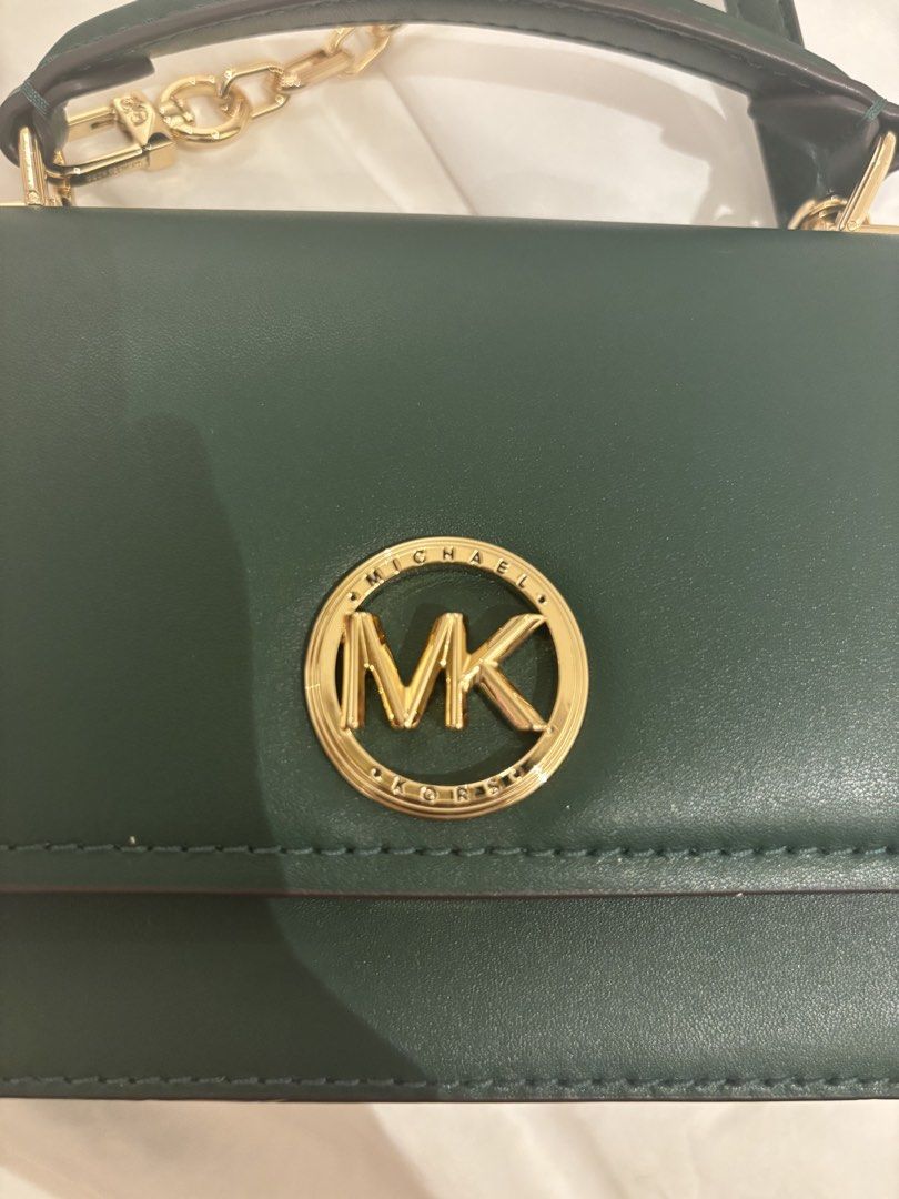 Michael Kors Green Leather Crossbody Bag (Category: Cross-body Bags) located in Quezon City. Submitted by kindakristelle2481 (Listing ID 1469878657, Image 2). Description: Dark green Michael Kors crossbody handbag with gold hardware. Circular MK logo on the front flap and square turn-lock closure. Adjustable strap and top handle included. Branded fabric lining inside with a Michael Kors logo tag. Includes white dust bag..