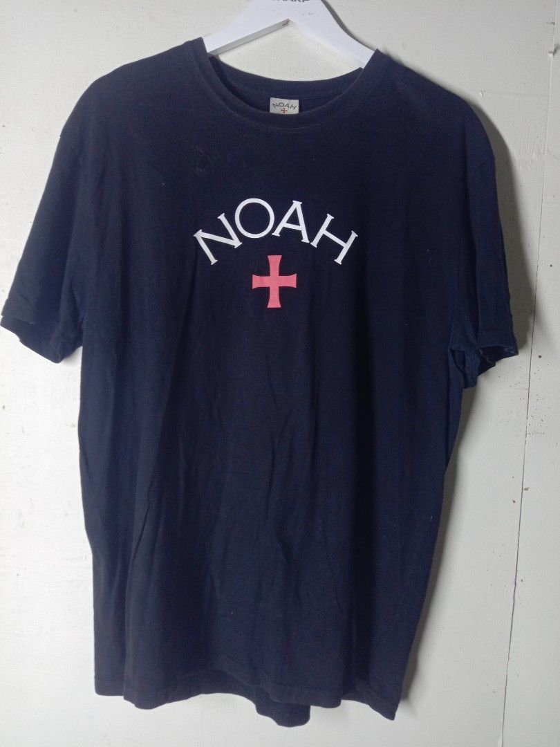 Noah NYC Cross Logo (Category: Tshirts & Polo Shirts ) located in Talavera. Submitted by cookiess. (Listing ID 1469892746, Image 1). Description: - Brand/Style: Noah navy blue t-shirt - Design: White arched branding with pink cross graphic on chest - Fit & Cut: Classic crewneck, short sleeves, regular fit - Details: Standard collar tag .