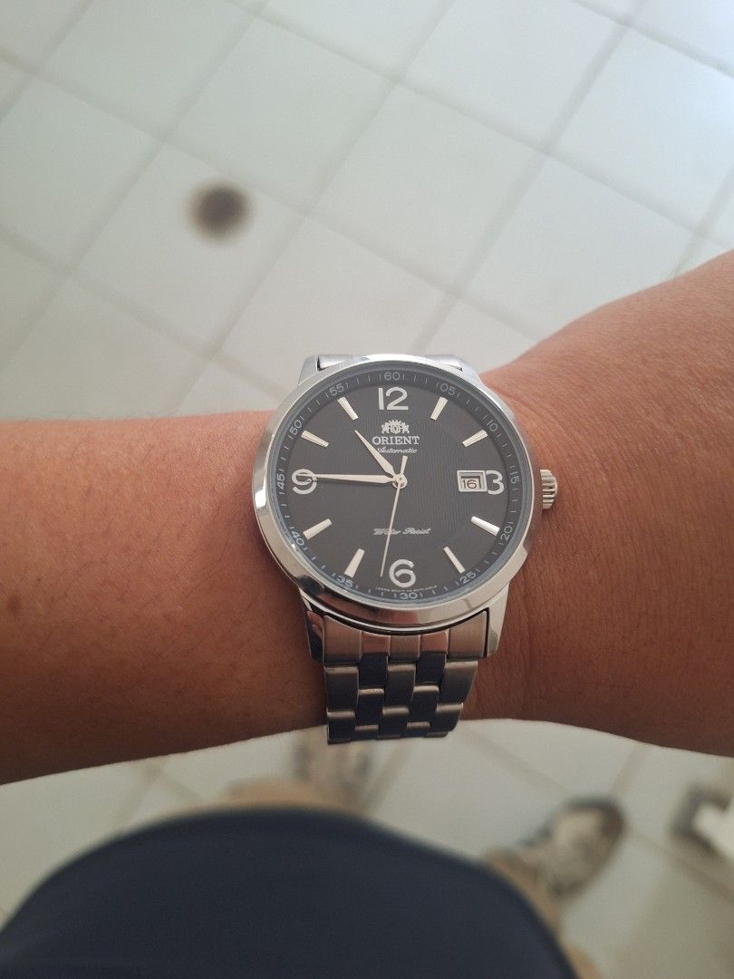 Orient Symphony watch (Category: Men's Watches) located in Manila. Submitted by caster_tee (Listing ID 1469828425, Image 2). Description: - Brand/Model: Orient Automatic Watch - Dial: Textured dark grey with silver-tone hands and markers - Numerals: Distinct Arabic numerals at 12 and 6 o'clock - Date Display: Convenient date window near the top right - Build: Stainless steel case and multi-row metal bracelet with signed clasp - Feature: Water res