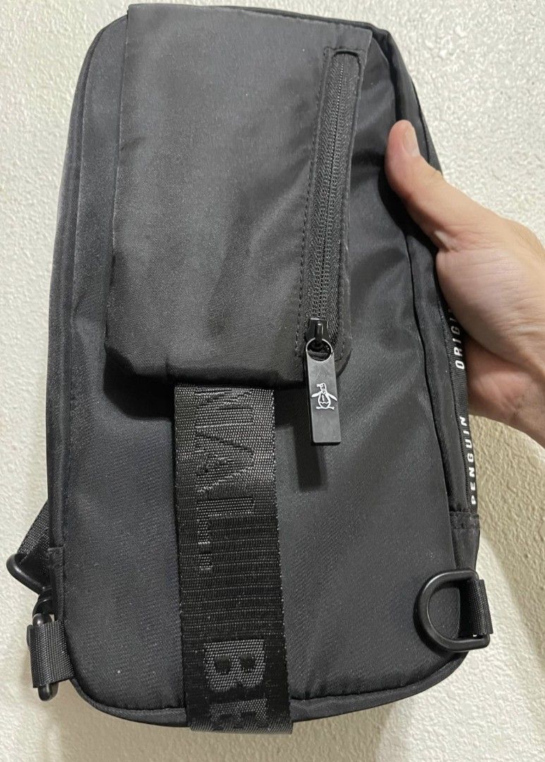 Original Penguin Black Crossbody Sling Bag (Category: Sling Bags) located in Malabon City. Submitted by neon.neon2 (Listing ID 1469908095, Image 3). Description: - Authentic Original Penguin black sling bag - Durable nylon material with branded text straps and zipper pulls - Front vertical white zipper compartment for quick access - Spacious main zip storage compartment - Adjustable strap for shoulder or crossbody wear - Clean condition with mini