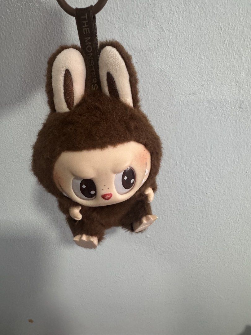 Pop Mart The Monsters Labubu Plush Pendant (Category: Plushies & Soft Toys) located in Manila. Submitted by decluterthings888 (Listing ID 1469827181, Image 1). Description: - Authentic Pop Mart The Monsters Labubu plush pendant - Adorable brown furry hood with cute bunny ears - Hard plastic face with painted eyes, red nose, and signature small fangs - Fabric loop strap featuring "THE MONSTERS" branding - Clean plush fabric with completely intact 