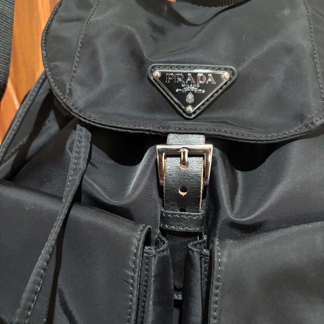 Prada Black Nylon Backpack (Category: Backpacks) located in Carmen. Submitted by ar_thrift00 (Listing ID 1469762693, Image 2). Description: - Brand: Prada - Material: Lightweight black nylon with silver-tone branded hardware - Design: Classic enamel triangle logo on the front flap - Closure: Drawstring main compartment with secure buckle strap - Storage: Dual exterior front pockets with flaps for easy access - Straps: Adjustable black webbed shou