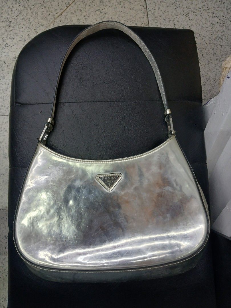 Prada Silver Shoulder Bag (Category: Luxury Bags & Wallets) located in Manila. Submitted by zackthrift16 (Listing ID 1469847834, Image 1). Description: - Brand: Prada - Color: Metallic silver - Style: Curved shoulder bag with single strap - Features: Front enamel triangle logo plaque, magnetic snap closure, and interior zip pocket with Prada Made in Italy metal plaque - Condition: Noticeable scuffs and surface wear on the metallic finish; hardwar