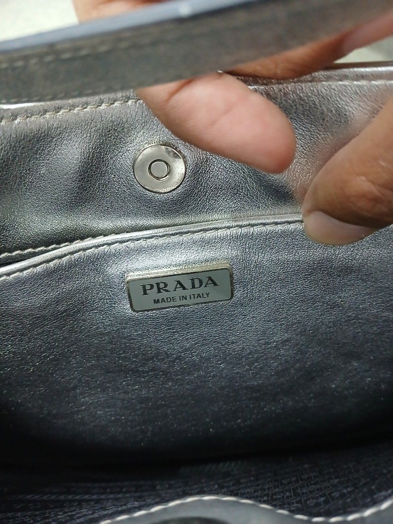 Prada Silver Shoulder Bag (Category: Luxury Bags & Wallets) located in Manila. Submitted by zackthrift16 (Listing ID 1469847834, Image 3). Description: - Brand: Prada - Color: Metallic silver - Style: Curved shoulder bag with single strap - Features: Front enamel triangle logo plaque, magnetic snap closure, and interior zip pocket with Prada Made in Italy metal plaque - Condition: Noticeable scuffs and surface wear on the metallic finish; hardwar