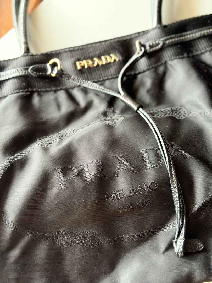 PRADA Tessuto Nylon Jacquard Logo Drawstring Tote Bag (Black) (Category: Luxury Bags & Wallets) located in Marikina City. Submitted by reloved8 (Listing ID 1469786521, Image 3). Description: - Brand: Prada - AUTHENTIC - Color: Classic black - Material: Durable nylon with glossy black handles - Hardware: Gold-tone Prada lettering on the top band - Design: Large embroidered logo on the front - Interior: Clean, roomy, and spacious - Condition: Ready