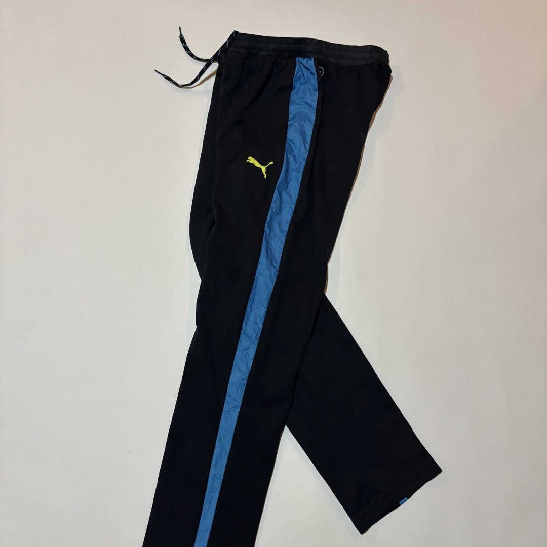 Puma Black Blue Track Pants Size L (Category: Joggers) located in Dipolog. Submitted by dionato (Listing ID 1469865330, Image 3). Description: - Brand: Puma - Color: Black with blue side stripes and neon yellow logo - Size: L (Tag attached) - Material: 100% polyester - Features: Elastic waistband with adjustable drawstring, and one zippered right pocket with a yellow-blue fade detail.