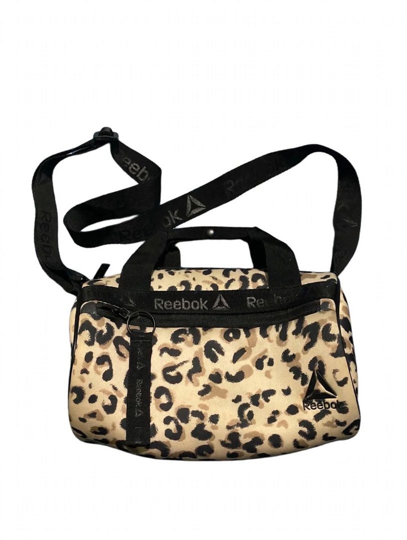 Reebok Leopard Print Crossbody Bag (Category: Cross-body Bags) located in Quezon City. Submitted by un0oo (Listing ID 1469923787, Image 1). Description: Reebok crossbody bag in a beige and black leopard print. Includes double top handles plus an adjustable shoulder strap with Reebok branding. Front zipper pocket with a matching logo pull tab, plus the Reebok triangle logo on the lower right corner. Spacious main compartment. Solid construction, c