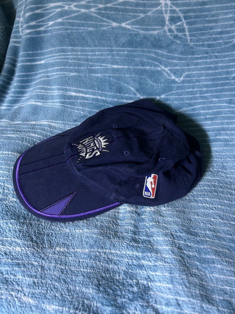 Sacramento Kings NBA Cap Hat (Category: Caps & Hats) located in Quezon City. Submitted by thriftxgoods (Listing ID 1469895546, Image 3). Description: - Color: Dark blue with purple accents - Team: Sacramento Kings (embroidered front logo) - Details: NBA side logo, unique vertical center stitching, and cut-out panels on the brim - Closure: Adjustable strap in the back for a custom fit - Condition: Clean fabric lining with original tags intact.