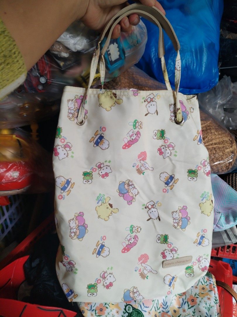 Sanrio Characters All-Over Print Tote Bag (Category: Tote Bags) located in La Trinidad. Submitted by malditas (Listing ID 1469918802, Image 1). Description: Cream-colored tote bag featuring an all-over print of various Sanrio characters including Kitty, Pompompurin, Little Twin Stars, and Keroppi. Dual top handles in a lighter neutral shade. Cream interior lining with an open slip pocket inside. Fabric tag reading Sanrio characters stitched near 