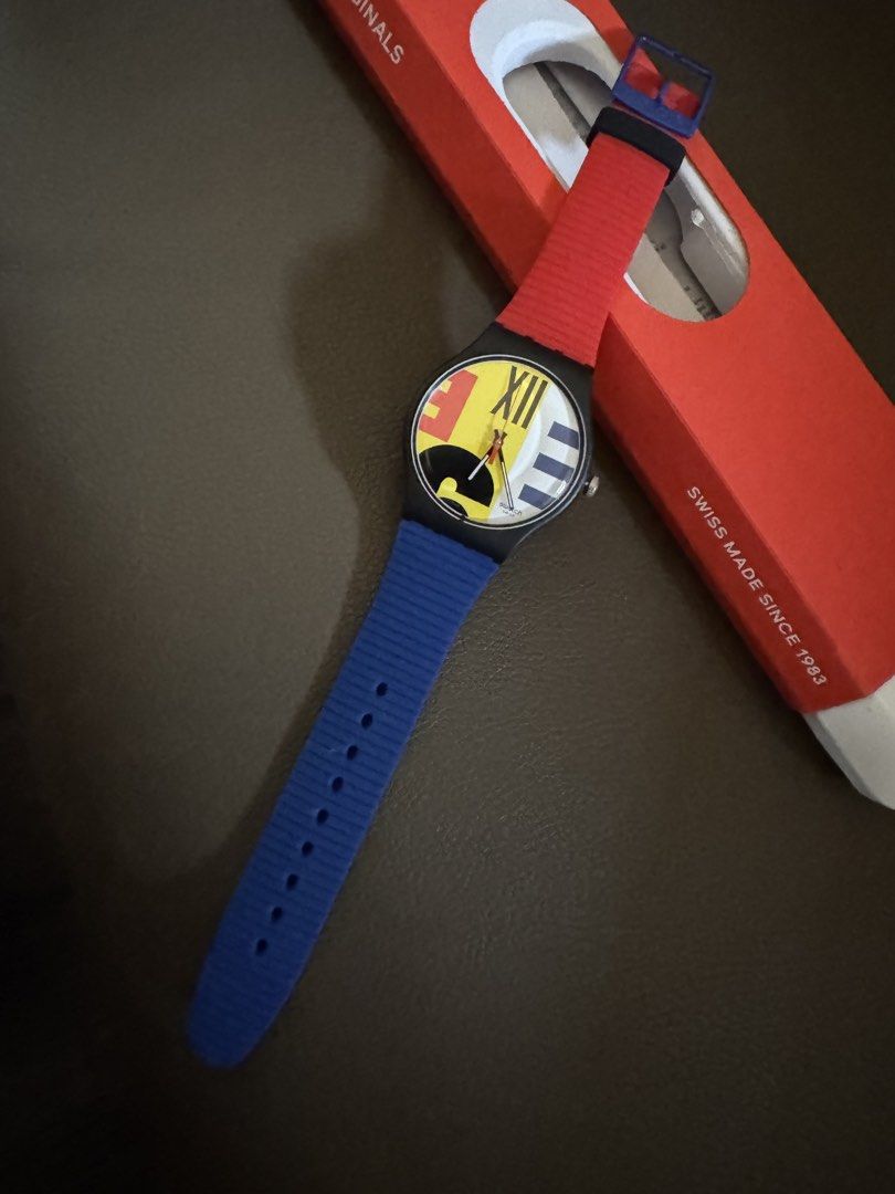 Swatch Abstract Limited Edition (Category: Men's Watches) located in Paranaque City. Submitted by sambautista88 (Listing ID 1469946524, Image 2). Description: - Brand: Swatch Originals - Design: Colorful retro statement piece with a vibrant dial, Roman numerals, and geometric shapes - Case: Black case with blue buckle clasp featuring the Swatch logo - Strap: Contrasting red and blue textured silicone straps - Inclusions: Original red Swatch box i