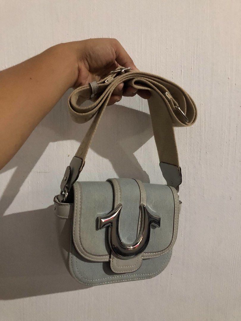 True Religion Sling Bag (Category: Cross-body Bags) located in Vigan. Submitted by chiyannav (Listing ID 1469869152, Image 2). Description: from US True Religion Mini Horseshoe Bag in a blue and grey/beige colorway. • Brand: True Religion • Style: Mini flap crossbody / shoulder bag with a prominent metallic horseshoe logo on the front flap • Material: Faux leather trim with denim/fabric body and an adjustable grosgrain strap.
