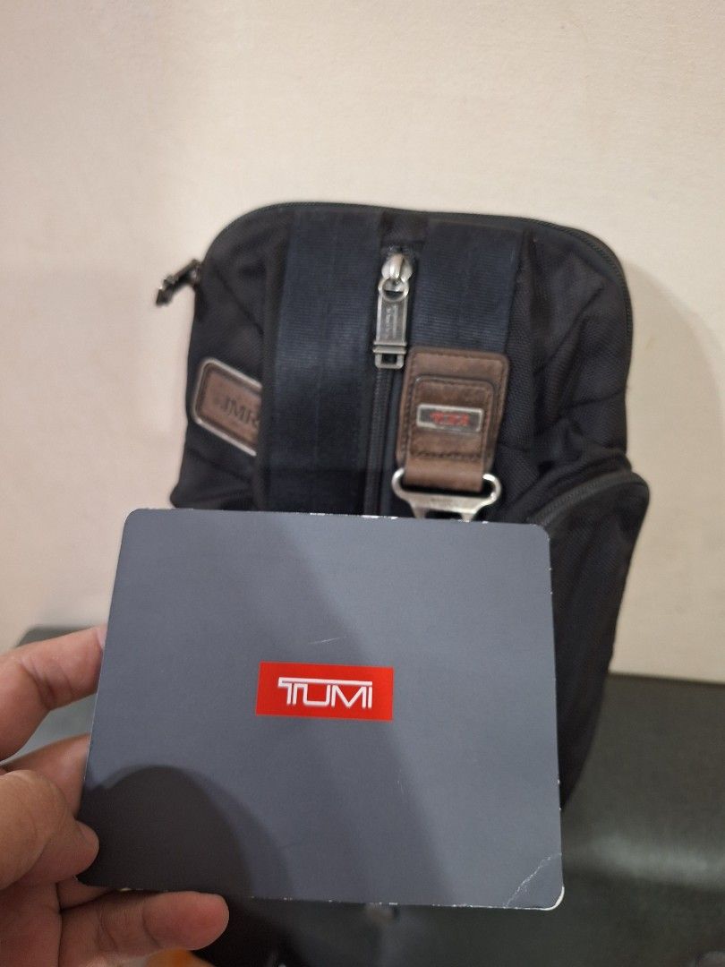 TUMI black and brown sling bag (Category: Sling Bags) located in Manila. Submitted by caster_tee (Listing ID 1469785730, Image 3). Description: - Authentic TUMI sling bag in classic black - Premium brown leather accents and hardware - Multiple secure zip compartments on front and top - Adjustable black strap with clasp hook detail - Interior features official TUMI leather brand tag - Includes original TUMI paper bag and booklet - Condition: Brand