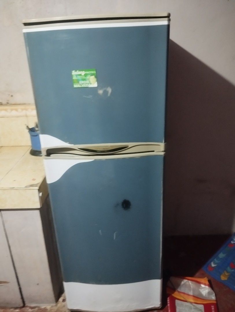 Two-door refrigerator with blue finish (Category: Refrigerators and Freezers) located in San Pedro. Submitted by jeome888 (Listing ID 1469882227, Image 1). Description: - Two-door refrigerator with a stylish dark blue and white finish - Features a contrasting beige handle latch in the middle and a small green sticker on the top corner - Shows cosmetic scuffs and marks on the outer body, with visible wear on the bottom white panel - Fully function
