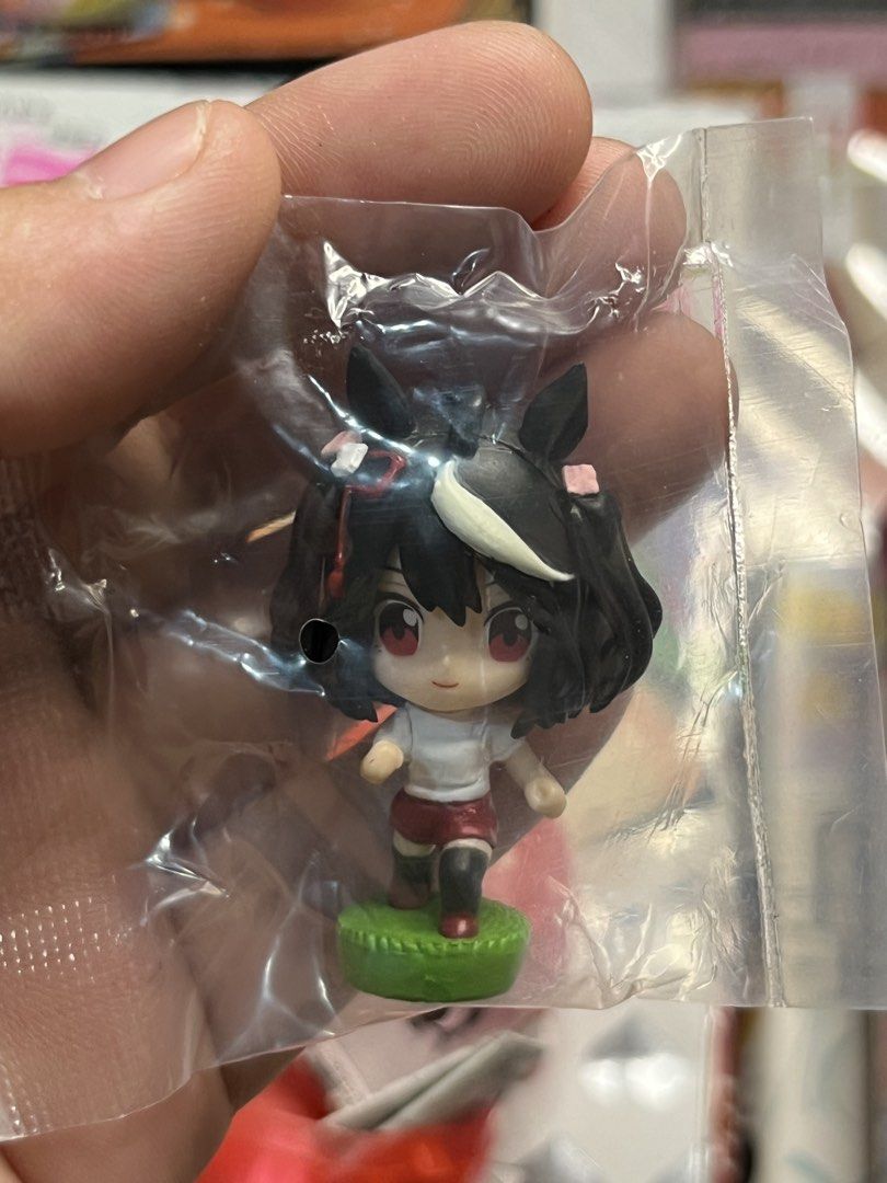 Umamusume Pretty Derby Capsule Figure (Category: Designer & Blind Box Toys) located in Gapan. Submitted by lunashop14 (Listing ID 1469799525, Image 2). Description: - Character: Tiny anime girl figurine with black/white hair, horse ears, and red eyes - Outfit/Base: Simple white top, red shorts, and green display base - Pose: Dynamic running pose - Condition: Brand new, pulled straight from the capsule machine - Packaging: Kept inside original pla
