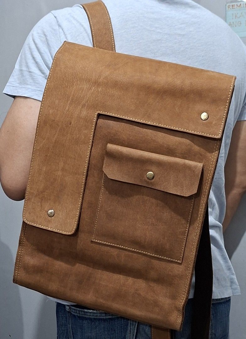 Vintage Brown Leather Backpack with Front Pocket (Category: Backpacks) located in Quezon City. Submitted by moonthrifting (Listing ID 1469888604, Image 2). Description: Tan genuine leather backpack with heavy distressing and visible grain. Asymmetric front flap with brass snap closure. Large exterior pocket with flap plus vertical zipper compartment on the back panel. Sturdy top grab handle and adjustable shoulder straps with canvas backing. Main
