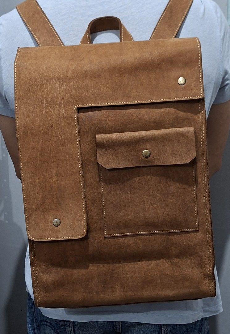 Vintage Brown Leather Backpack with Front Pocket (Category: Backpacks) located in Quezon City. Submitted by moonthrifting (Listing ID 1469888604, Image 1). Description: Tan genuine leather backpack with heavy distressing and visible grain. Asymmetric front flap with brass snap closure. Large exterior pocket with flap plus vertical zipper compartment on the back panel. Sturdy top grab handle and adjustable shoulder straps with canvas backing. Main