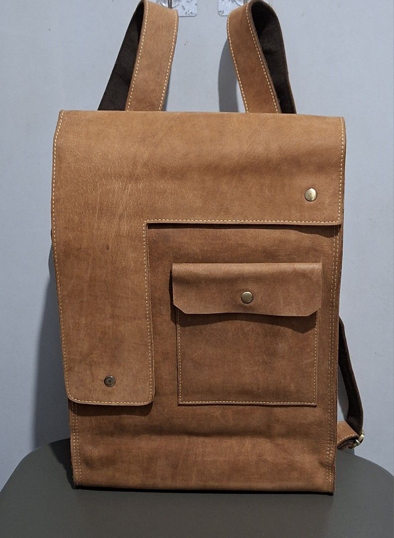 Vintage Brown Leather Backpack with Front Pocket (Category: Backpacks) located in Quezon City. Submitted by moonthrifting (Listing ID 1469888604, Image 3). Description: Tan genuine leather backpack with heavy distressing and visible grain. Asymmetric front flap with brass snap closure. Large exterior pocket with flap plus vertical zipper compartment on the back panel. Sturdy top grab handle and adjustable shoulder straps with canvas backing. Main