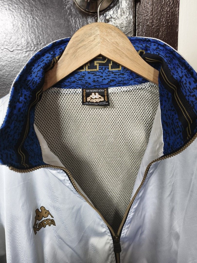 Vintage Kappa White Track Jacket Size XO (Category: Coats, Jackets and Outerwear) located in Manila. Submitted by ian.frias_ (Listing ID 1469837831, Image 3). Description: White Kappa track jacket with black ribbed cuffs and hem. Gold embroidery details on the chest and sleeves, plus colorful patterned panels on the arms. High collar featuring blue knit lining with large Kappa lettering. Mesh lining inside. Full front zip with zip pockets. Japane