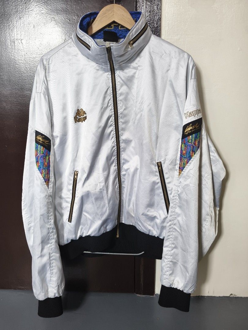 Vintage Kappa White Track Jacket Size XO (Category: Coats, Jackets and Outerwear) located in Manila. Submitted by ian.frias_ (Listing ID 1469837831, Image 1). Description: White Kappa track jacket with black ribbed cuffs and hem. Gold embroidery details on the chest and sleeves, plus colorful patterned panels on the arms. High collar featuring blue knit lining with large Kappa lettering. Mesh lining inside. Full front zip with zip pockets. Japane