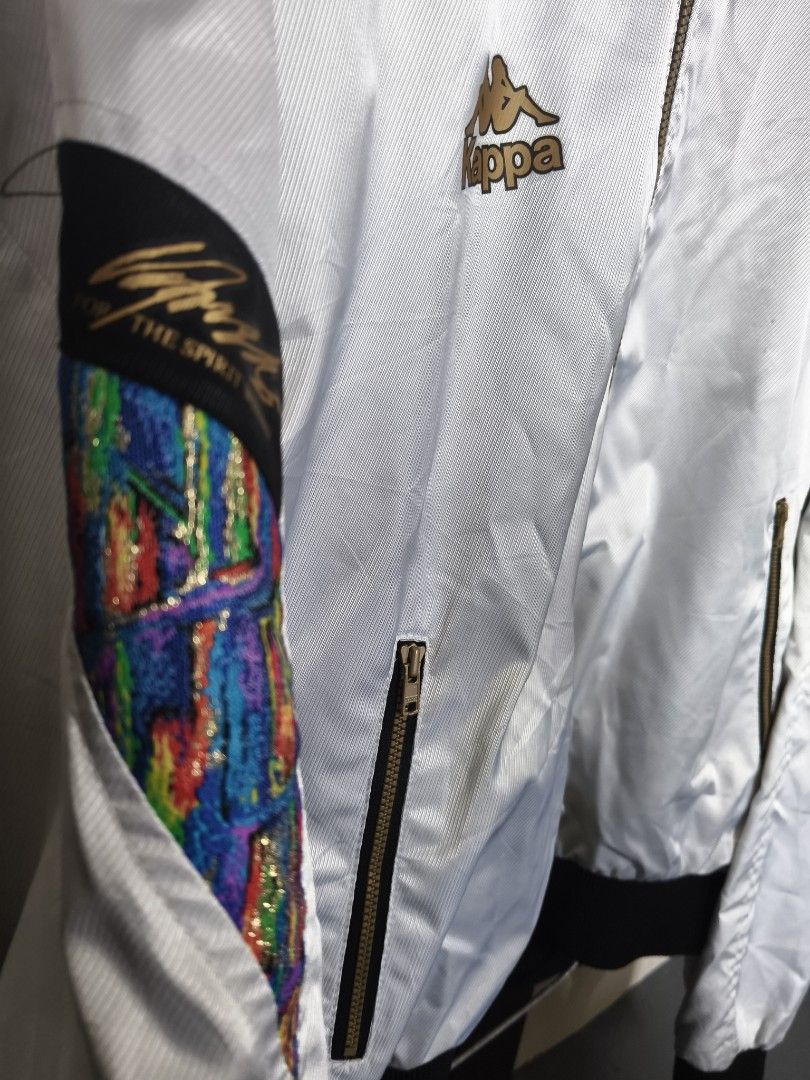 Vintage Kappa White Track Jacket Size XO (Category: Coats, Jackets and Outerwear) located in Manila. Submitted by ian.frias_ (Listing ID 1469837831, Image 2). Description: White Kappa track jacket with black ribbed cuffs and hem. Gold embroidery details on the chest and sleeves, plus colorful patterned panels on the arms. High collar featuring blue knit lining with large Kappa lettering. Mesh lining inside. Full front zip with zip pockets. Japane