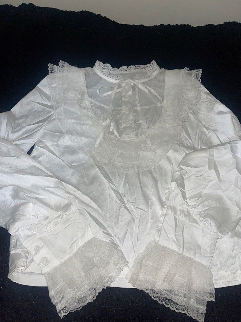White lace trim ruffle blouse long sleeve (Category: Longsleeves) located in La Trinidad. Submitted by potatothriftlip (Listing ID 1469871120, Image 1). Description: - Style: Romantic vintage, ideal for Lolita and Gothic fashion - Design: Button-up front with a soft satin-like body fabric - Details: Sheer mesh neckline, delicate lace collar, and tiered lace cuffs - Accents: Includes a matching ribbon tie at the collar - Condition: Brand new/Mint 