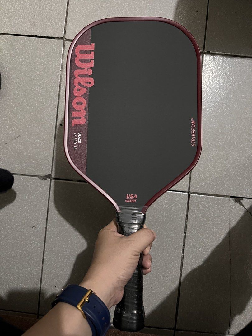 Wilson Blaze SF Pro 13 Pickleball Paddle (Category: Racket and Ball Sports) located in Quezon City. Submitted by pickleballpaddle (Listing ID 1469770341, Image 2). Description: - Brand/Model: Wilson Blaze SF Pro 13 pickleball paddle - Colorway: Stylish dark grey and red - Face Technology: Integrated StrikeFoam for enhanced performance - Certification: Official USA Pickleball approved stamp near the throat - Handle: Wrapped in premium black grip t