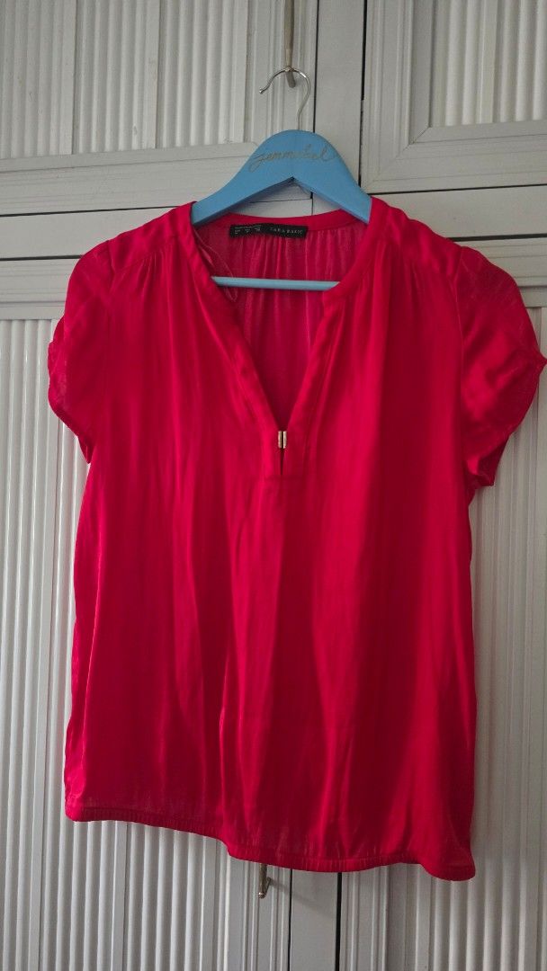 Zara Basic Red Short Sleeve Blouse (Category: Blouses) located in Cabanatuan. Submitted by belle_1013 (Listing ID 1469947099, Image 2). Description: - Brand: Zara Basic - Color: Bright red - Style: Short sleeve V-neck blouse with metallic clasp detail - Fabric: Lightweight and comfortable for warm weather - Versatility: Easy to pair with trousers for work or jeans for casual wear - Condition: Clean, with tags intact inside the collar.