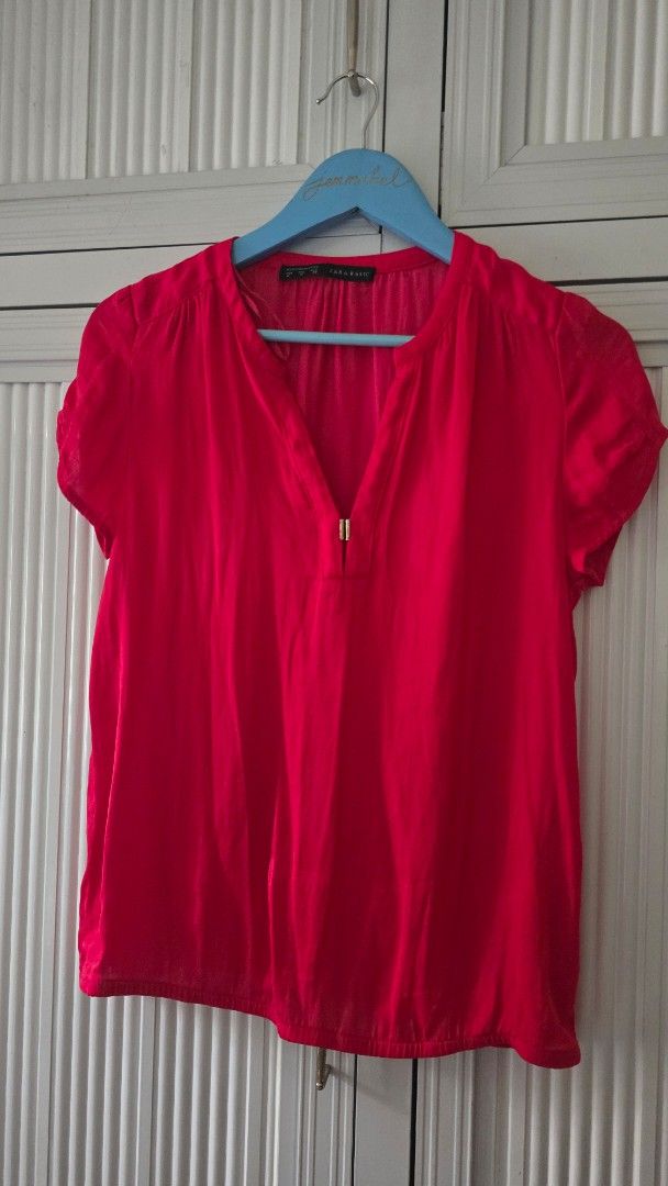 Zara Basic Red Short Sleeve Blouse (Category: Blouses) located in Cabanatuan. Submitted by belle_1013 (Listing ID 1469947099, Image 1). Description: - Brand: Zara Basic - Color: Bright red - Style: Short sleeve V-neck blouse with metallic clasp detail - Fabric: Lightweight and comfortable for warm weather - Versatility: Easy to pair with trousers for work or jeans for casual wear - Condition: Clean, with tags intact inside the collar.