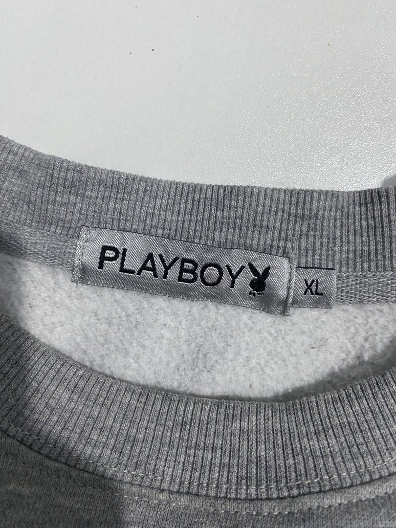 90s Playboy Grey Crewneck Sweatshirt (Category: Coats, Jackets and Outerwear) located in San Pablo. Submitted by gt_vault (Listing ID 1470124801, Image 2). Description: Ready to wear Width: Length: Color rate: 9/10 Condition: Excellent Issue: None - Size: XL - Color: Grey - Small embroidered Playboy logo on the chest - Bold black branding and tiny bunny graphics down both sleeves - Ribbed collar, cuffs, and hem - Thick fleece lining for extra war