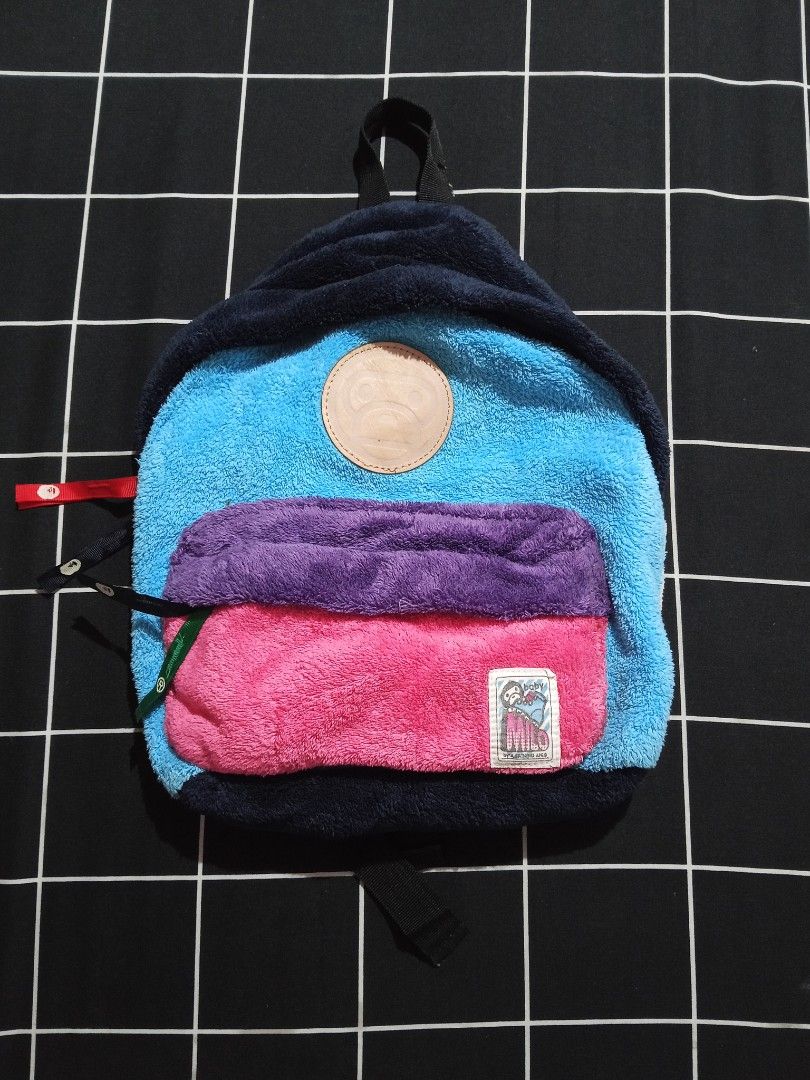 A Bathing Ape Baby Milo Multi-color Plush Backpack (Category: Backpacks) located in Glan. Submitted by cpaharodde48008 (Listing ID 1470115917, Image 1). Description: - Brand: Baby Milo by A Bathing Ape (Made in Japan) - Material: Cozy multi-color fleece fabric (navy, blue, purple, pink) - Pockets: Front zipper pocket with woven Milo character label - Details: Debossed leather monkey logo patch, stylish ribbon side pull tabs, and interior gold Ape