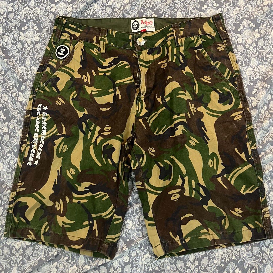 AAPE By A Bathing Ape Camo Cargo Shorts (Category: Shorts) located in Batangas. Submitted by gavsandrix (Listing ID 1470139350, Image 1). Description: - Brand: AAPE by A Bathing Ape - Design: Classic green, brown, and tan camouflage pattern - Graphics: Large white ape head skull on back right leg and vertical text print on right front pocket - Pockets: Multiple functional pockets with secure button closures - Details: Branded woven tags on waistb