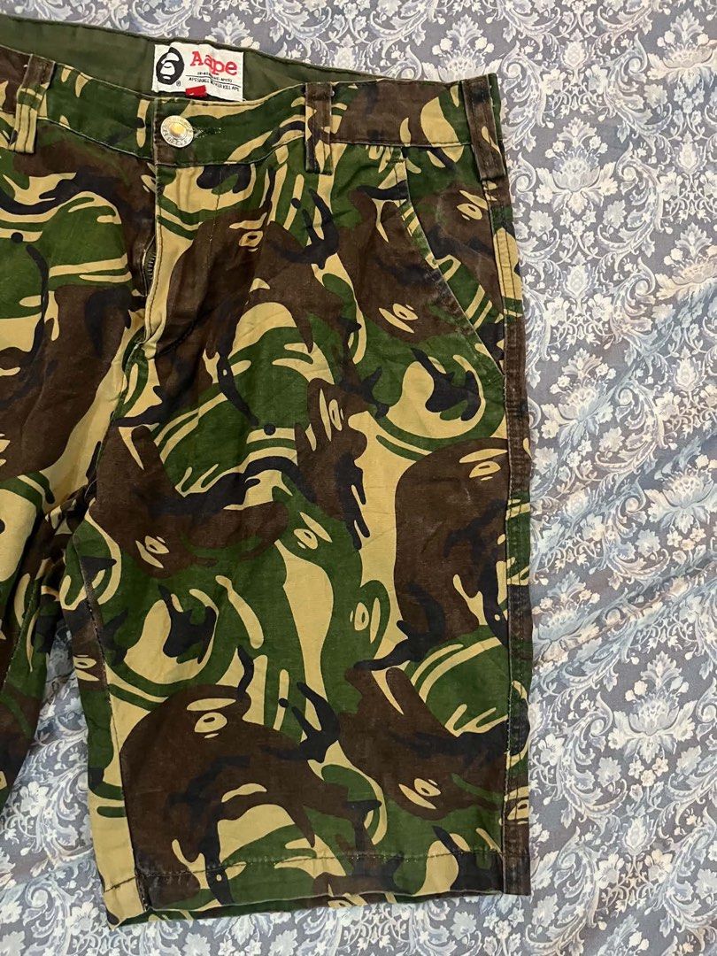 AAPE By A Bathing Ape Camo Cargo Shorts (Category: Shorts) located in Batangas. Submitted by gavsandrix (Listing ID 1470139350, Image 3). Description: - Brand: AAPE by A Bathing Ape - Design: Classic green, brown, and tan camouflage pattern - Graphics: Large white ape head skull on back right leg and vertical text print on right front pocket - Pockets: Multiple functional pockets with secure button closures - Details: Branded woven tags on waistb