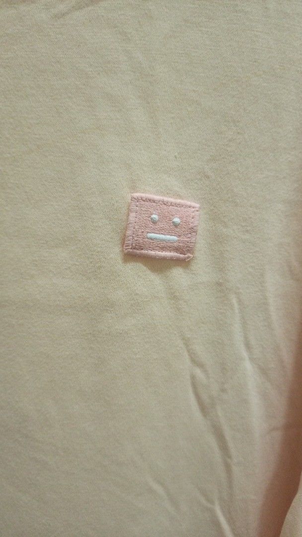 Acne Studios Face Patch Peach T-Shirt (Category: Activewear) located in Manila. Submitted by rizu09 (Listing ID 1470040080, Image 3). Description: - Brand: Acne Studios - Color: Peach (Neutral pastel tone) - Design: Iconic pink face logo patch on left chest - Fit: Relaxed fit with short sleeves - Material: 100% soft cotton for comfortable daily wear - Details: Black interior neck brand label - Condition: Excellent / As described - Mode of payment