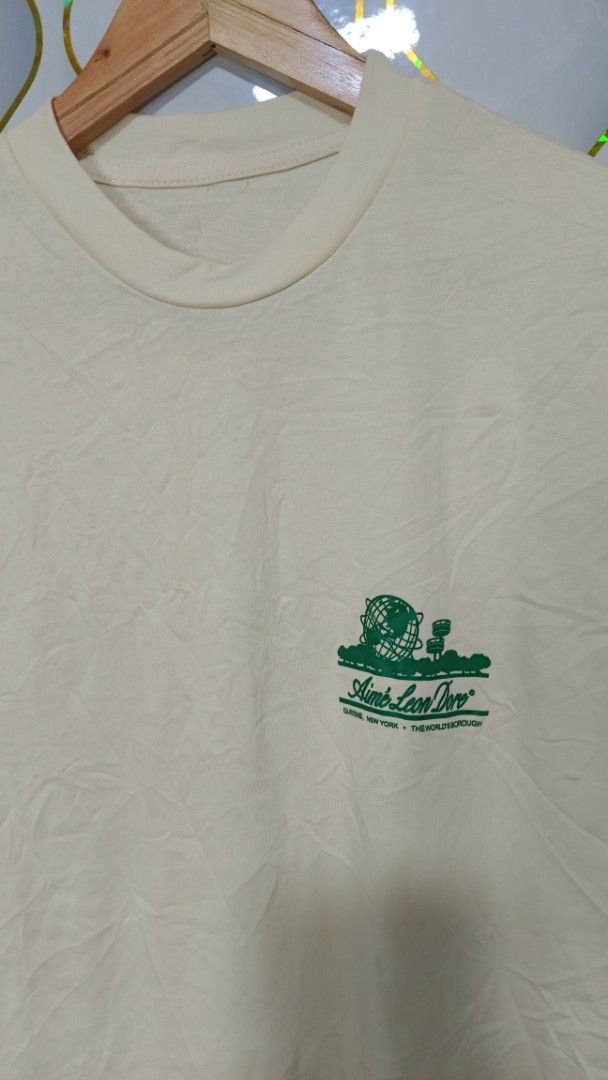 Aimé Leon Dore Queens World's Borough Tee (Category: Tshirts & Polo Shirts ) located in Manila. Submitted by zariyah.1986 (Listing ID 1469950106, Image 2). Description: - Brand: Aimé Leon Dore - Color: Cream with green graphic print - Design: Small chest logo and large back graphic featuring the Queens Unisphere and landmarks - Details: Crew neck, short sleeves, clean collar - Measurements: 21.5 inches pit to pit, 28.5 inches length - Condition: 