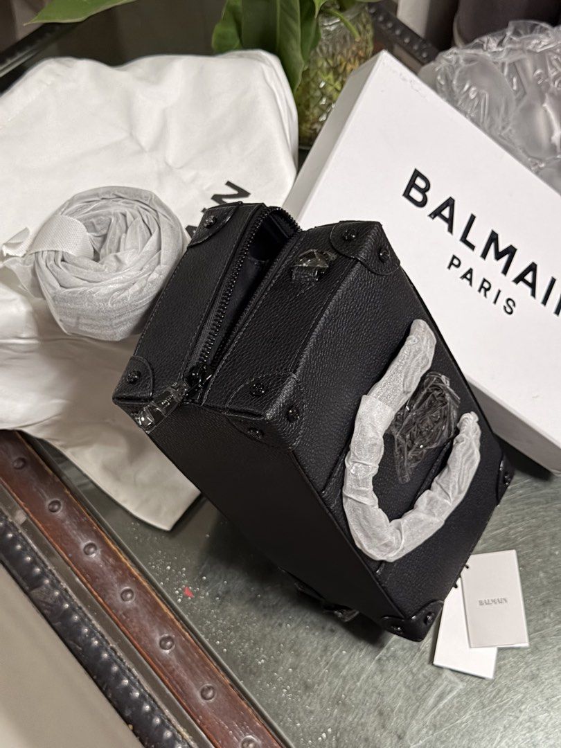 Balmain Paris Black Leather Trunk Handbag (Category: Luxury Bags & Wallets) located in Marilao. Submitted by lindyaneza (Listing ID 1469952950, Image 2). Description: - Brand: Balmain Paris - Color/Material: Black grained leather - Style: Structured trunk bag with reinforced corners - Features: Double top handles, top zip closure, and detachable shoulder strap - Condition: Brand new, protective wrapping still attached to hardware and handles - In