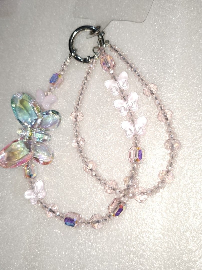 Beaded Phone Charm Wrist Strap (Category: Charms) located in Caloocan City. Submitted by books_and_beads (Listing ID 1470081662, Image 2). Description: - Handmade multi-strand beaded wrist strap - Features cute butterfly, rose, and rocking horse pendants: · Left Chain: A truly ethereal, fairy-princess design. It features a massive, iridescent mermaid-core butterfly alongside delicate rose-pink butterfly charms, all strung on a translucent pink be