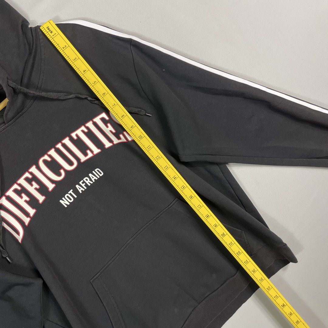 Black DIFFICULTIES Graphic Hoodie Unisex Size Medium (Category: Hoodies) located in Norzagaray. Submitted by sevenjscloset (Listing ID 1470015849, Image 3). Description: - Color: Black with striped sleeves - Design: 'DIFFICULTIES NOT AFRAID' graphic text on the front - Size: Medium (Length: 25 inches, Width: 18.5 inches) - Condition: Minimal fade on the front hood and base area, barely noticeable when worn - Fit reference: Model is 5'10 and weigh