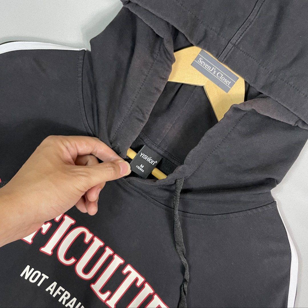 Black DIFFICULTIES Graphic Hoodie Unisex Size Medium (Category: Hoodies) located in Norzagaray. Submitted by sevenjscloset (Listing ID 1470015849, Image 2). Description: - Color: Black with striped sleeves - Design: 'DIFFICULTIES NOT AFRAID' graphic text on the front - Size: Medium (Length: 25 inches, Width: 18.5 inches) - Condition: Minimal fade on the front hood and base area, barely noticeable when worn - Fit reference: Model is 5'10 and weigh