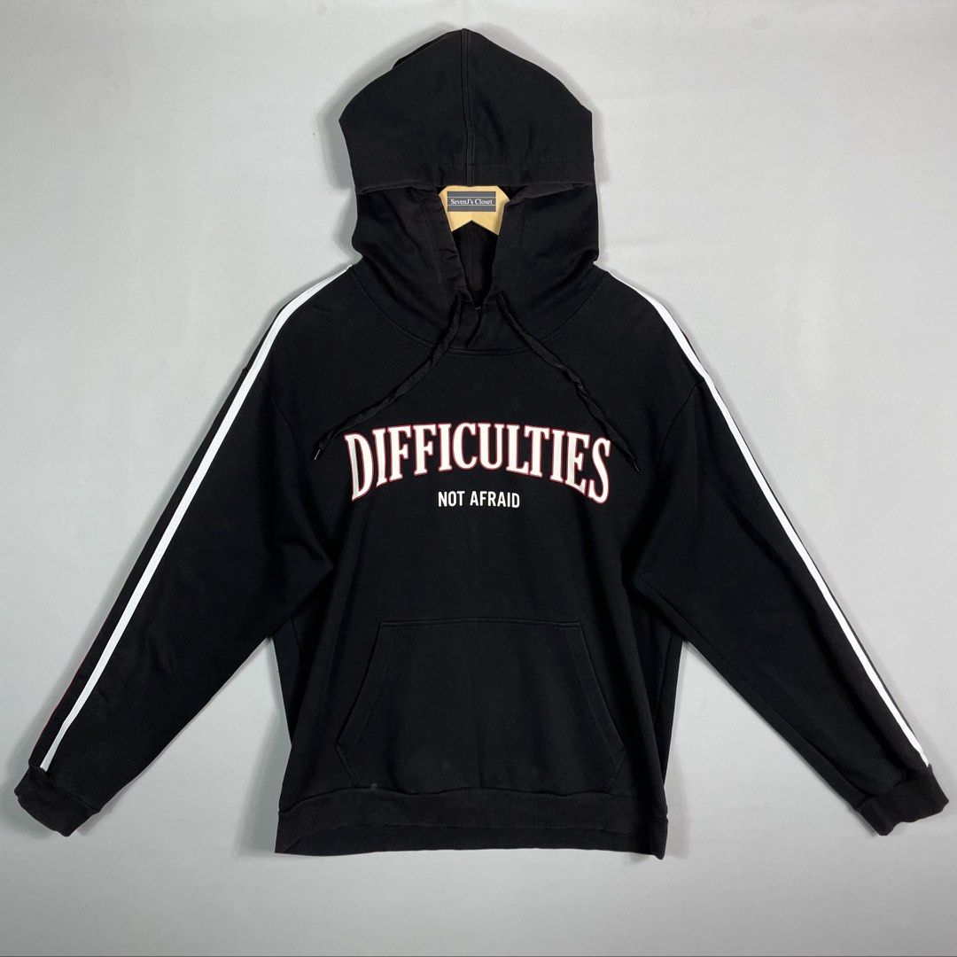 Black DIFFICULTIES Graphic Hoodie Unisex Size Medium (Category: Hoodies) located in Norzagaray. Submitted by sevenjscloset (Listing ID 1470015849, Image 1). Description: - Color: Black with striped sleeves - Design: 'DIFFICULTIES NOT AFRAID' graphic text on the front - Size: Medium (Length: 25 inches, Width: 18.5 inches) - Condition: Minimal fade on the front hood and base area, barely noticeable when worn - Fit reference: Model is 5'10 and weigh