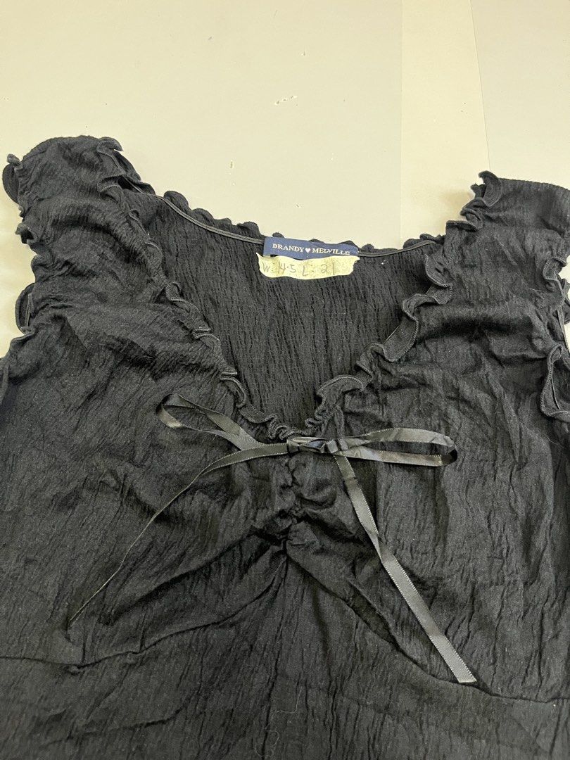 Brandy Melville Black Ruffle Bow Tank Top (Category: Sleeveless) located in Mabalacat. Submitted by aas_thriftfings (Listing ID 1470105655, Image 2). Description: - Brand: Brandy Melville - Color: Black - Material: 55% cotton, 42% polyamide, 3% spandex (lightweight & stretchable) - Design: Crinkled texture with V-neckline, delicate ruffles, and capped sleeves - Detail: Cute center-front satin bow accent - Care: Machine washable - Condition: Brand