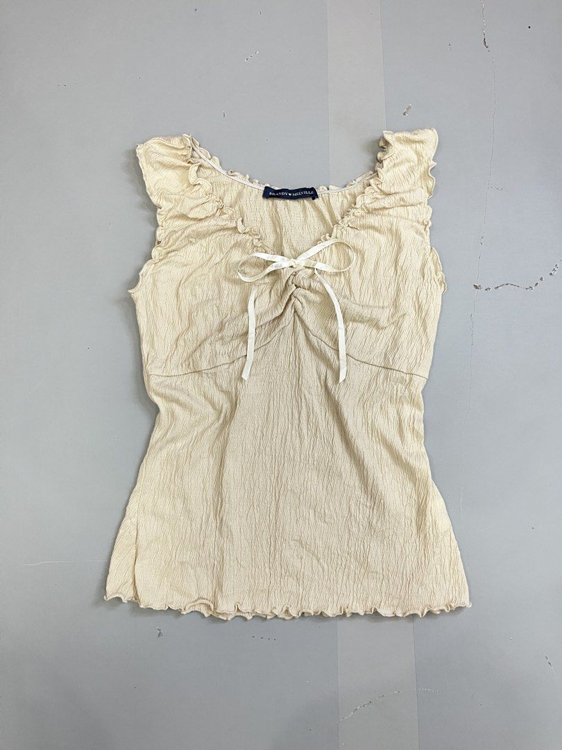 Brandy Melville Cream Ruffled Bow Tank Top (Category: Sleeveless) located in Mabalacat. Submitted by aas_thriftfings (Listing ID 1470105657, Image 1). Description: - Brand: Brandy Melville - Color: Cream - Fabric: Textured crinkle material (55% cotton, 42% polyester, 3% spandex) - Details: Lettuce trim edges, scoop neck, and a cute little white ribbon at the center front bust - Condition: Excellent, no flaws spotted - Care: Machine wash max 30 de