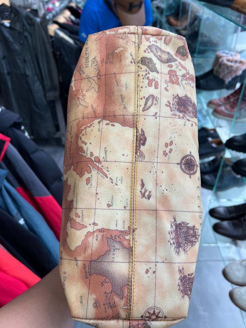 Bufall Vintage Map Print Tote Bag (Category: Tote Bags) located in Urdaneta. Submitted by jayceegarage (Listing ID 1470096007, Image 3). Description: Tan tote bag covered in an old-world map graphic. Brown leather shoulder straps and matching trim. Top zip closure keeps stuff secure. Inside lining is brown fabric with a zipper pocket. Structured bottom panel. Zipper pull has the Bufall logo stamped on it. Clean interior stuffed with plastic bags 