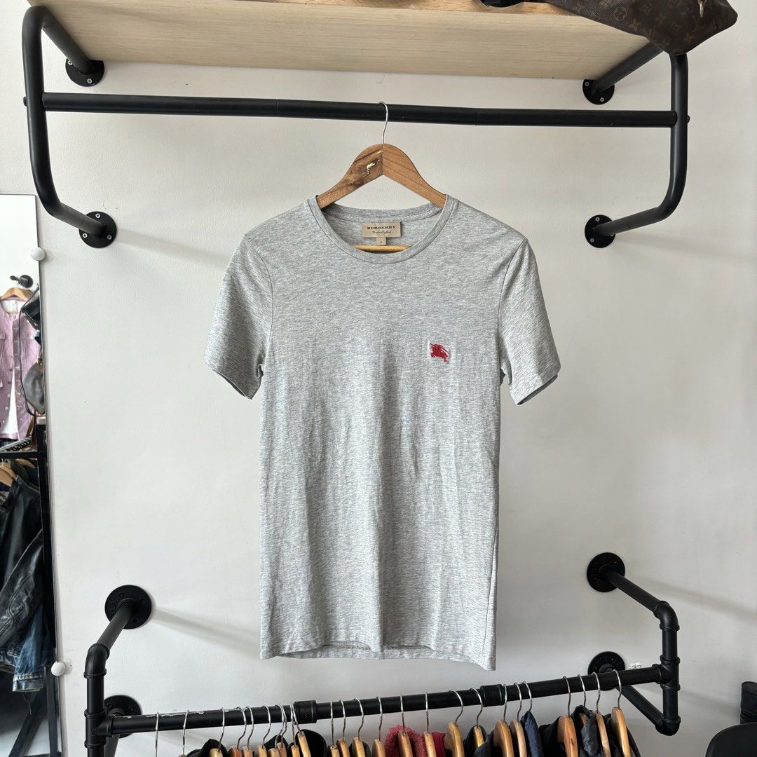 Burberry Grey T-Shirt Size M (Category: Shirts) located in Bambang. Submitted by heats777 (Listing ID 1470019100, Image 2). Description: - Brand: Burberry London England - Item: Grey short-sleeve t-shirt with crew neckline - Detail: Small red embroidered equestrian knight logo on left chest - Size: Tagged Medium (M) - Material: 100% Cotton, Made in China - Condition: Clean piece with minimal signs of wear - Style: Solid luxury basic for daily rot