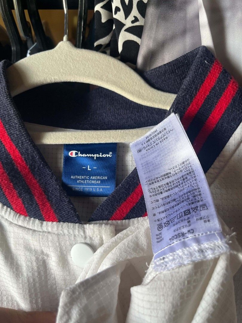 Champion White Varsity Jacket Size L (Category: Coats, Jackets and Outerwear) located in Tuguegarao City. Submitted by ZeevLim (Listing ID 1470080862, Image 3). Description: - Brand: Champion - Style: Snap-button varsity jacket - Color: White with red and blue ribbed collar, cuffs, and hem - Details: Bold arched chenille lettering across the chest - Material: Lightweight grid-texture fabric with front slip pockets and adjustable drawstring hem - 