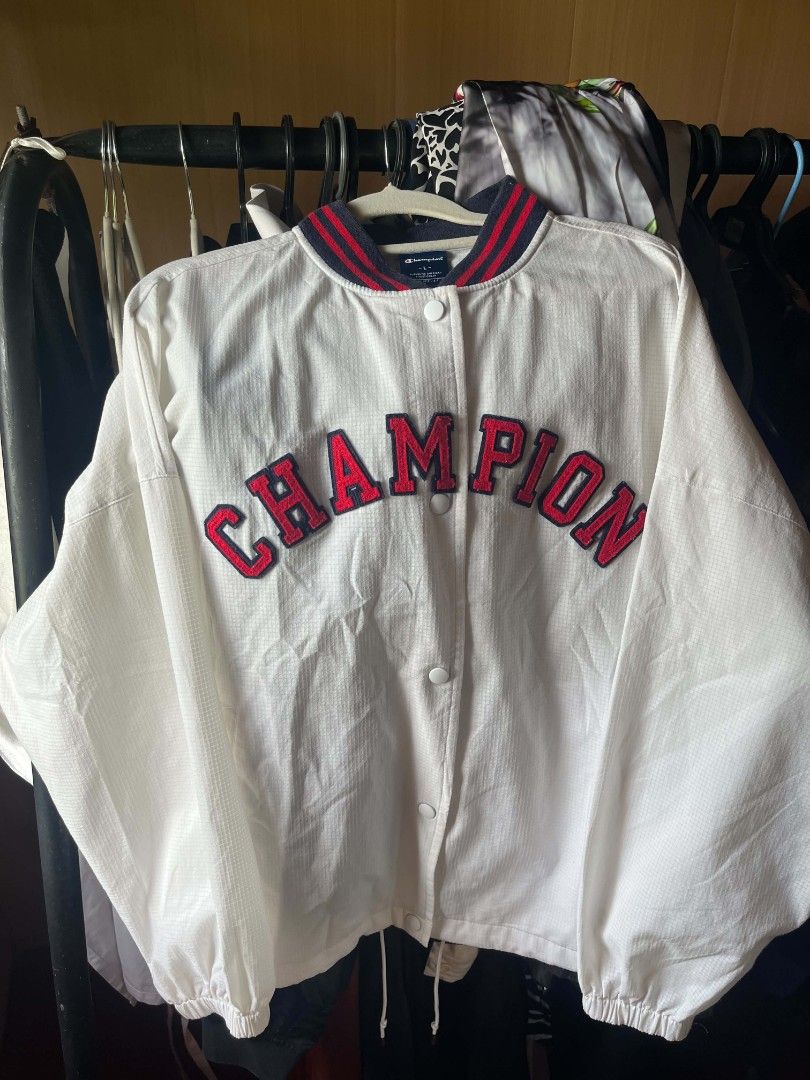 Champion White Varsity Jacket Size L (Category: Coats, Jackets and Outerwear) located in Tuguegarao City. Submitted by ZeevLim (Listing ID 1470080862, Image 2). Description: - Brand: Champion - Style: Snap-button varsity jacket - Color: White with red and blue ribbed collar, cuffs, and hem - Details: Bold arched chenille lettering across the chest - Material: Lightweight grid-texture fabric with front slip pockets and adjustable drawstring hem - 