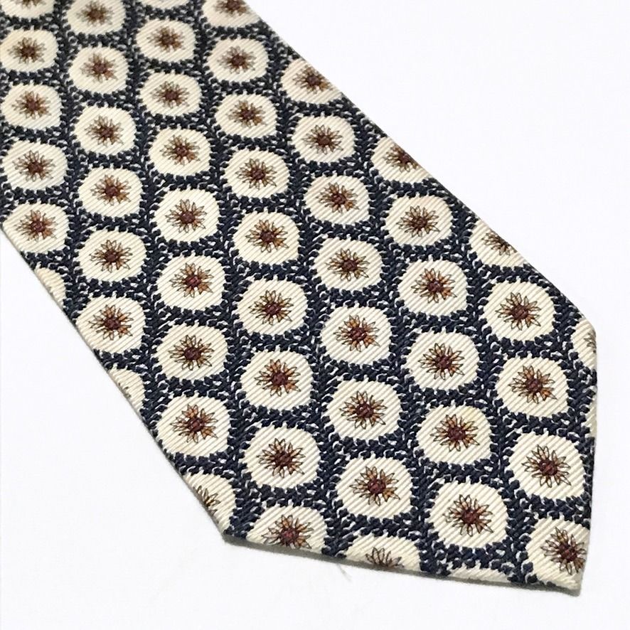 Christian Dior Repeating Floral Pattern Neck Tie (Category: Ties) located in Taguig. Submitted by retrogaze (Listing ID 1470080152, Image 2). Description: This 100% silk necktie by Christian Dior features an off-white cream base with a soft horizontal ribbed repp texture. The body is decorated with an ornate repeating geometric lattice pattern of dark navy blue leafy garlands framing starburst-like floral starburst motifs in warm rust-orange and 