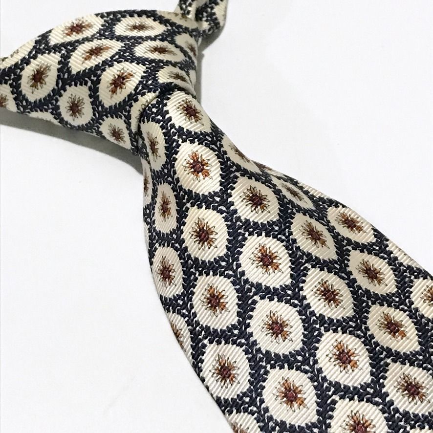 Christian Dior Repeating Floral Pattern Neck Tie (Category: Ties) located in Taguig. Submitted by retrogaze (Listing ID 1470080152, Image 1). Description: This 100% silk necktie by Christian Dior features an off-white cream base with a soft horizontal ribbed repp texture. The body is decorated with an ornate repeating geometric lattice pattern of dark navy blue leafy garlands framing starburst-like floral starburst motifs in warm rust-orange and 